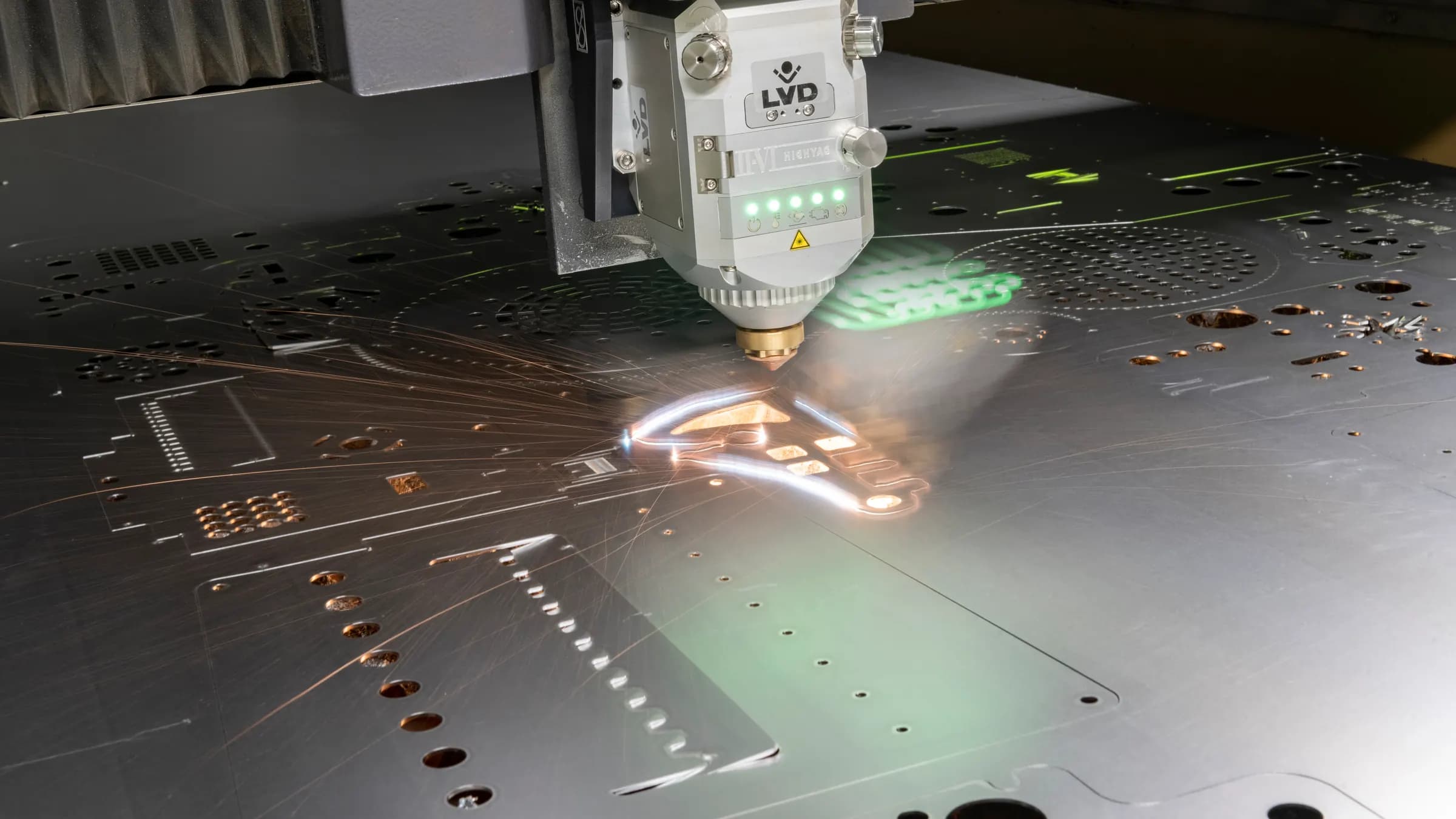 An LVD fibre laser cutting head cutting a steel sheet, sparks flaring from the cut line
